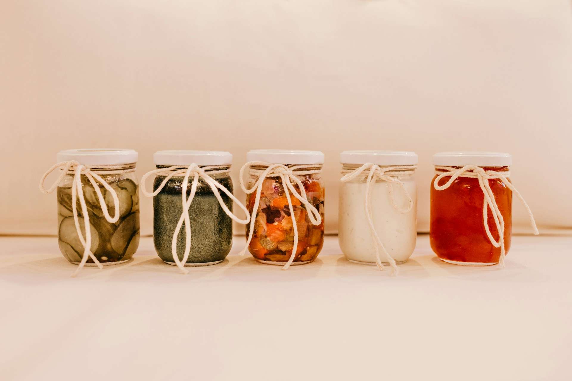 Five glass jars containing different food products, arranged in a row on a neutral surface.